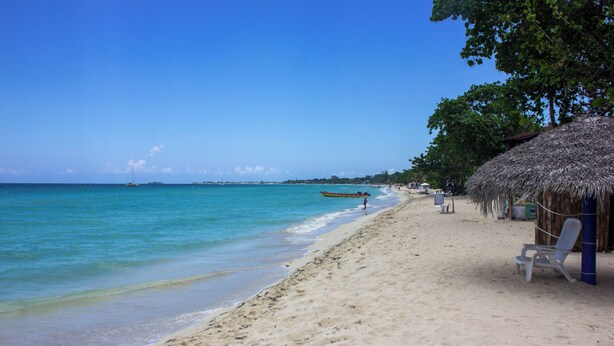 A beach with a thatched-roof hut, a row of beach chairs, and a boat in the water. - Barry's Rooms Negril (Negril)