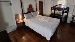 A bedroom with a wooden bed, a nightstand with a lamp, a wooden dresser, and a mirror. - Barry's Rooms Negril (Negril)