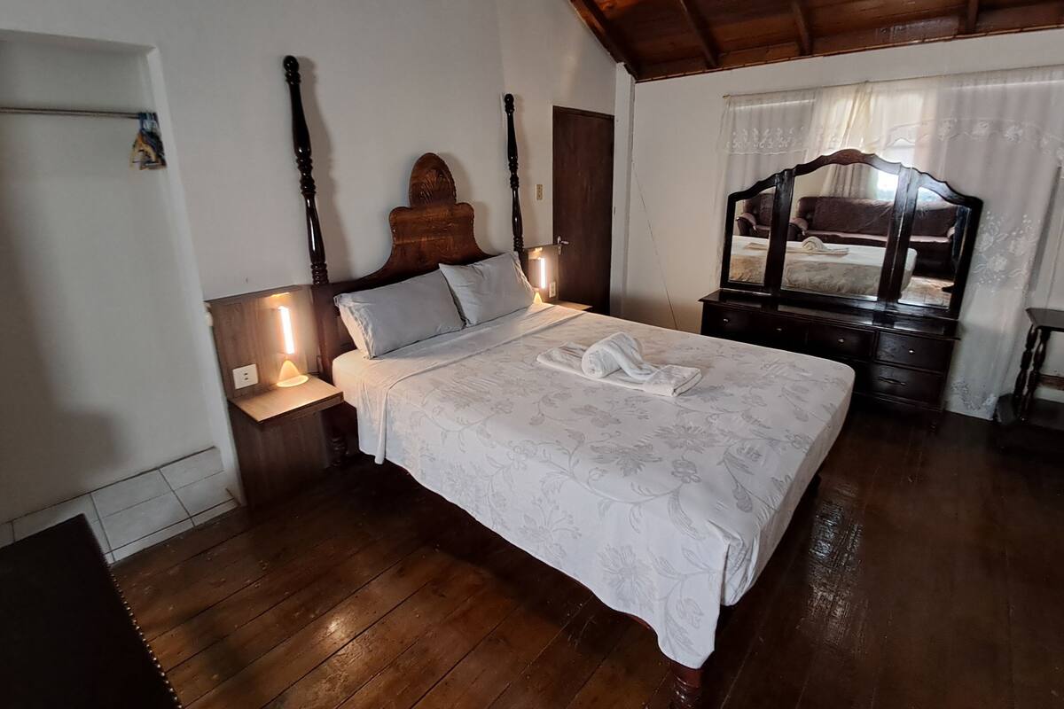 Ein Schlafzimmer mit einem hölzernen Bett, einem Nachttisch mit Lampe, einer Holzkommode und einem Spiegel.
