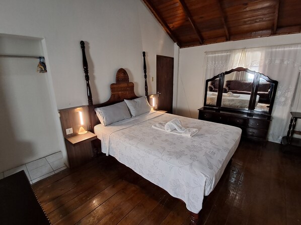 Une chambre à coucher avec un lit en bois, une table de chevet avec une lampe, une commode en bois et un miroir.