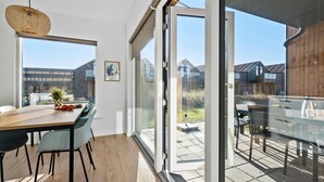 A modern interior with a wooden table, chairs, a hanging light, and a glass door leading to an outdoor patio.