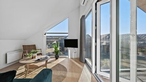 A modern living room with a large sliding glass door, a flat-screen TV mounted on the wall, a round coffee table, a sofa, and a chair.