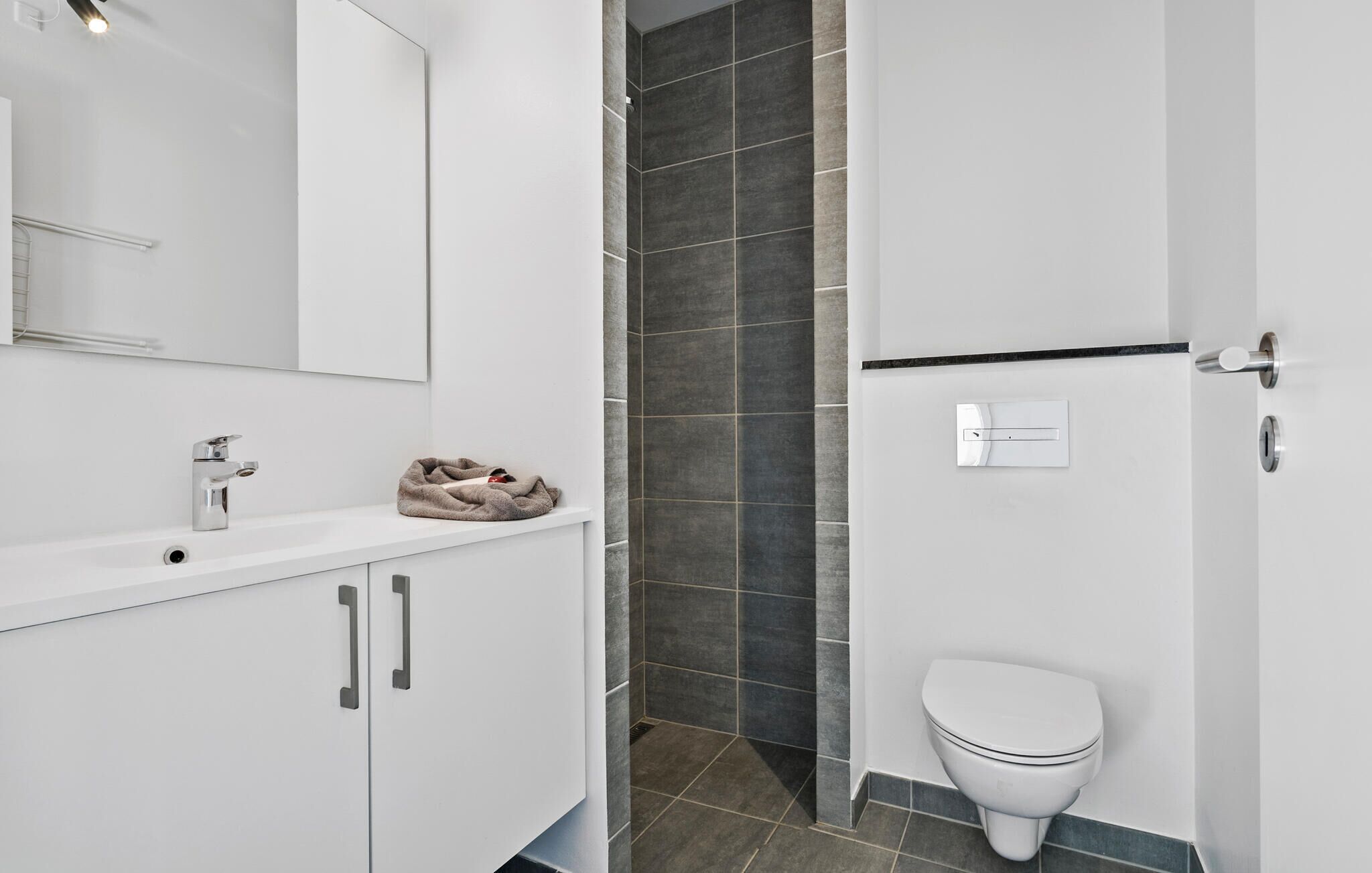 A modern bathroom with a white vanity, a towel rack, a toilet, and a shower area with dark tiles.