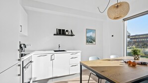 A modern kitchen with white cabinetry, a wooden dining table, and a view of a building through a large window.