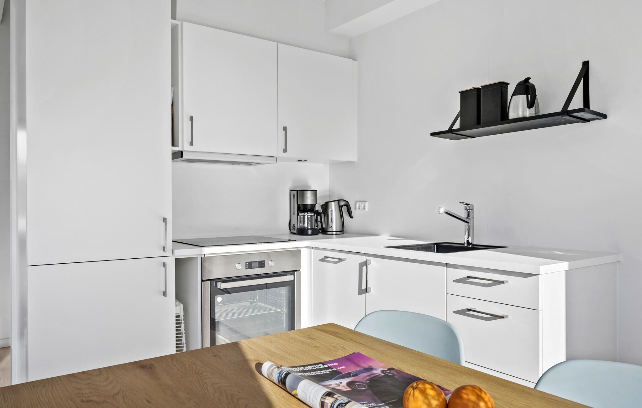 A modern kitchen with white cabinetry, a built-in oven, a coffee maker, and a sink.