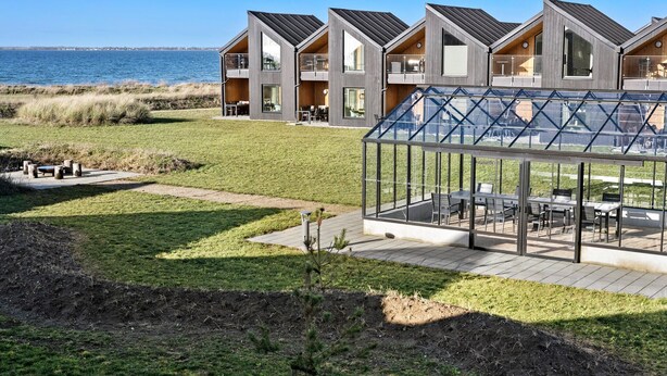 A modern residential building with a glass conservatory, a grassy lawn, and a view of the sea.