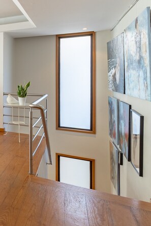 Ein modernes Interieur mit einer Holztreppe, einer weißen Wand mit abstrakter Kunst und einer Topfpflanze.