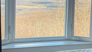 A room with a large window offering a view of a forested landscape. - Beau Ridge Cabin (Little Cabin with a big view) (Linden)