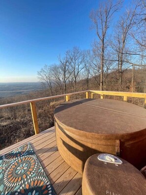 A wooden deck with a hot tub, a patterned rug, and a view of the landscape.