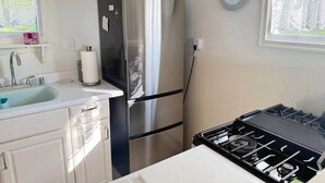 A compact kitchen with a stainless steel refrigerator, a sink, a stove, and a clock on the wall. - Beau Ridge Cabin (Little Cabin with a big view) (Linden)