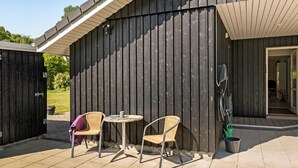 Ein Patio mit zwei Korbstühlen, einem kleinen runden Tisch, einem Holzzaun und einer zur Innenseite führenden Tür.