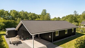 Ein eingeschossiges Gebäude mit geneigtem Dach, einer überdachten Veranda und einer kleinen angebauten Garage.