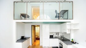 A modern kitchen with white cabinets, a microwave, and a dining area with a wooden table and chairs. - Giovio Duplex Apartment (Milano)