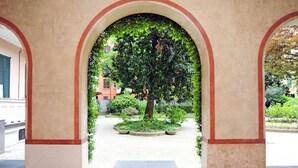 An arched entrance with a tree in the center, a tiled floor, and a building in the background. - Giovio Duplex Apartment (Milano)