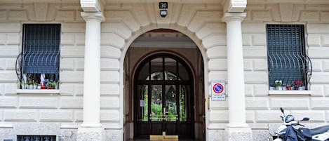 A building entrance with a number '30' above the door, a no-parking sign, and a scooter parked outside.