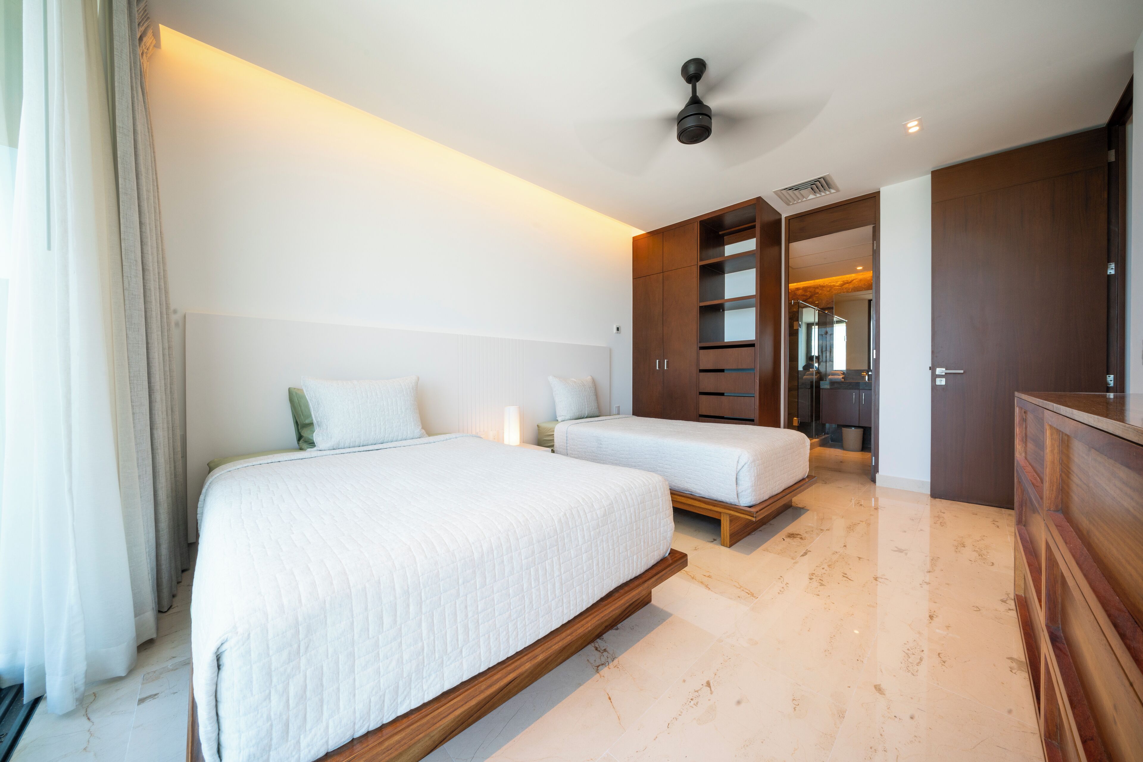 A modern hotel room with a large bed, a smaller bed, a wardrobe, and a ceiling fan.