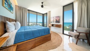 A modern bedroom with a large bed, a TV, and a view of the ocean. - Marila - Luxury 3 BR - Ocean View & Pool (Playa del Carmen)