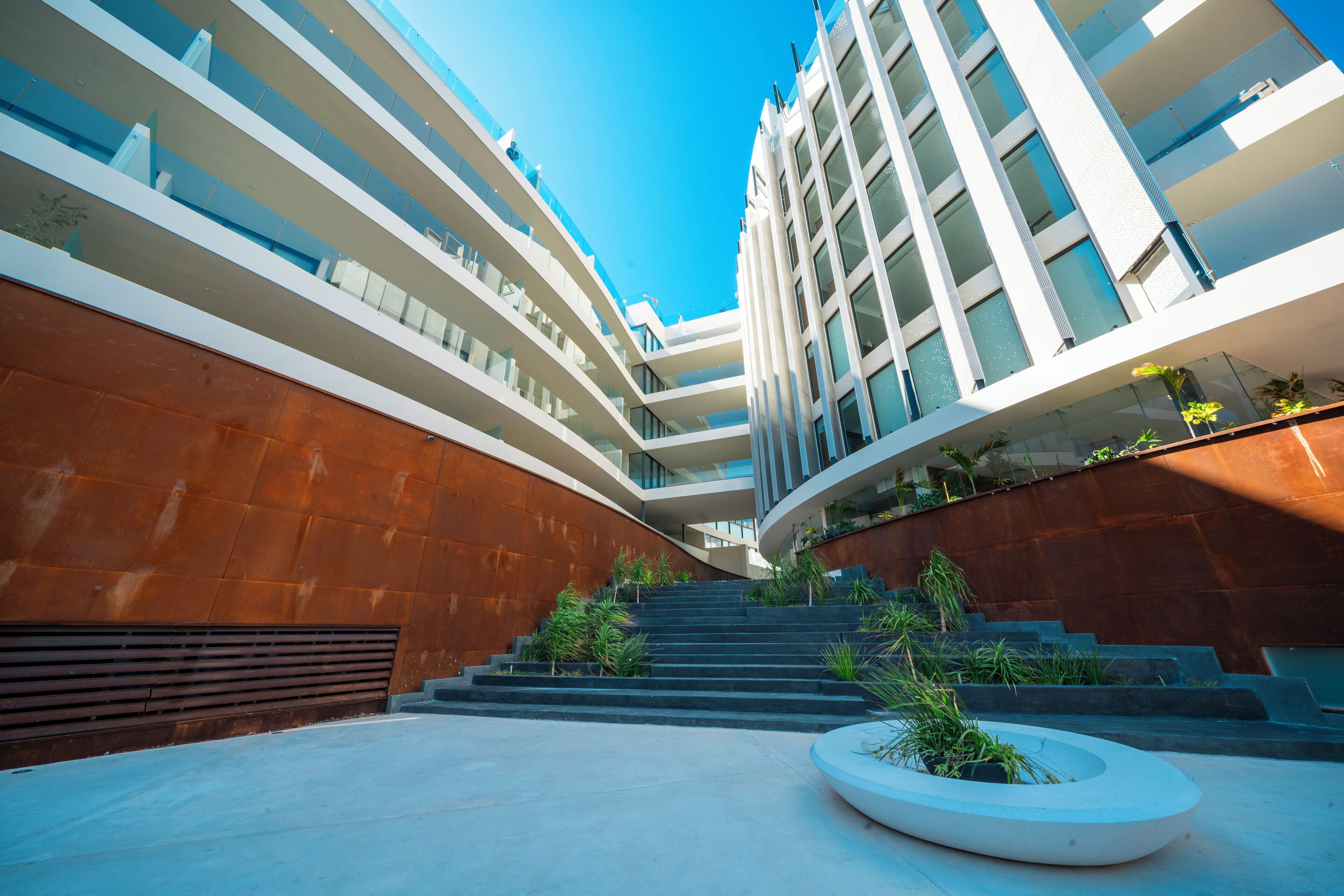 Een modern gebouw met meerdere verdiepingen, een centrale trap en een ronde plantenbak met beplanting.