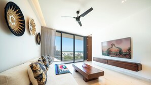 A modern living room with a sofa, a coffee table, a ceiling fan, and a large window offering a city view. - Marila - Luxury 3 BR - Ocean View & Pool (Playa del Carmen)