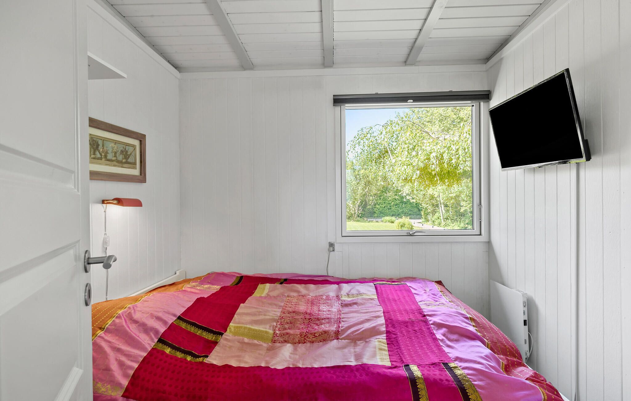 Een slaapkamer met een bed, een raam, een deur en een aan de muur bevestigde televisie.