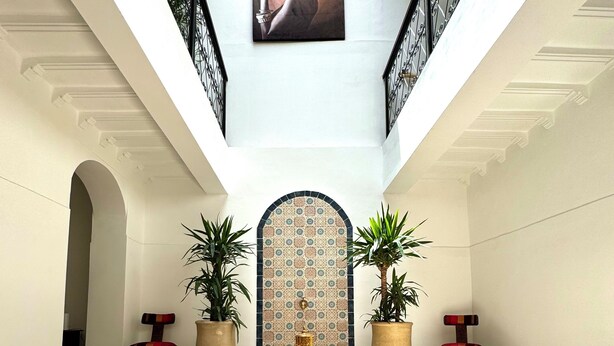 Un hall d’entrée spacieux avec un plafond haut, un mur décoratif central et un escalier.