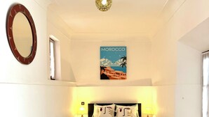 Une chambre à coucher avec un lit, des lampes de chevet, un luminaire suspendu, une affiche, un miroir et une fenêtre.