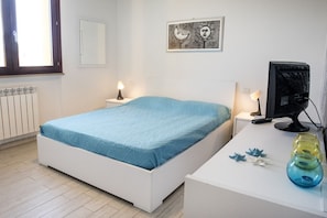 A bedroom with a bed, bedside tables, a desk, a computer, and decorative items.