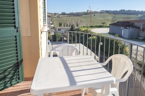 A balcony with a white table and chairs, a view of the countryside, and a green door.