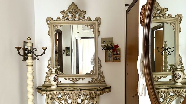 Un espejo con un marco ornamentado, un candelabro y un jarrón pequeño sobre una consola.
