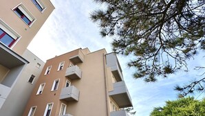 Un edificio de varios pisos con balcones, cielo despejado y algo de vegetación.