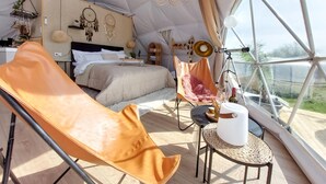 Una tenda espaiosa amb un llit, una cadira relaxant, un telescopi i vista a l'exterior.
