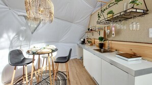 Cuina compacta amb zona de menjador, amb llum penjant, prestatge de fusta amb plantes i una petita barra.