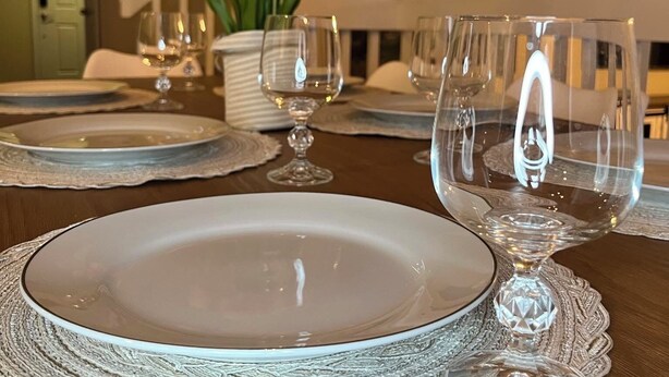 Una mesa de comedor dispuesta con platos blancos y cristalería transparente, un jarrón con tulipanes anaranjados y un cuadro al fondo.