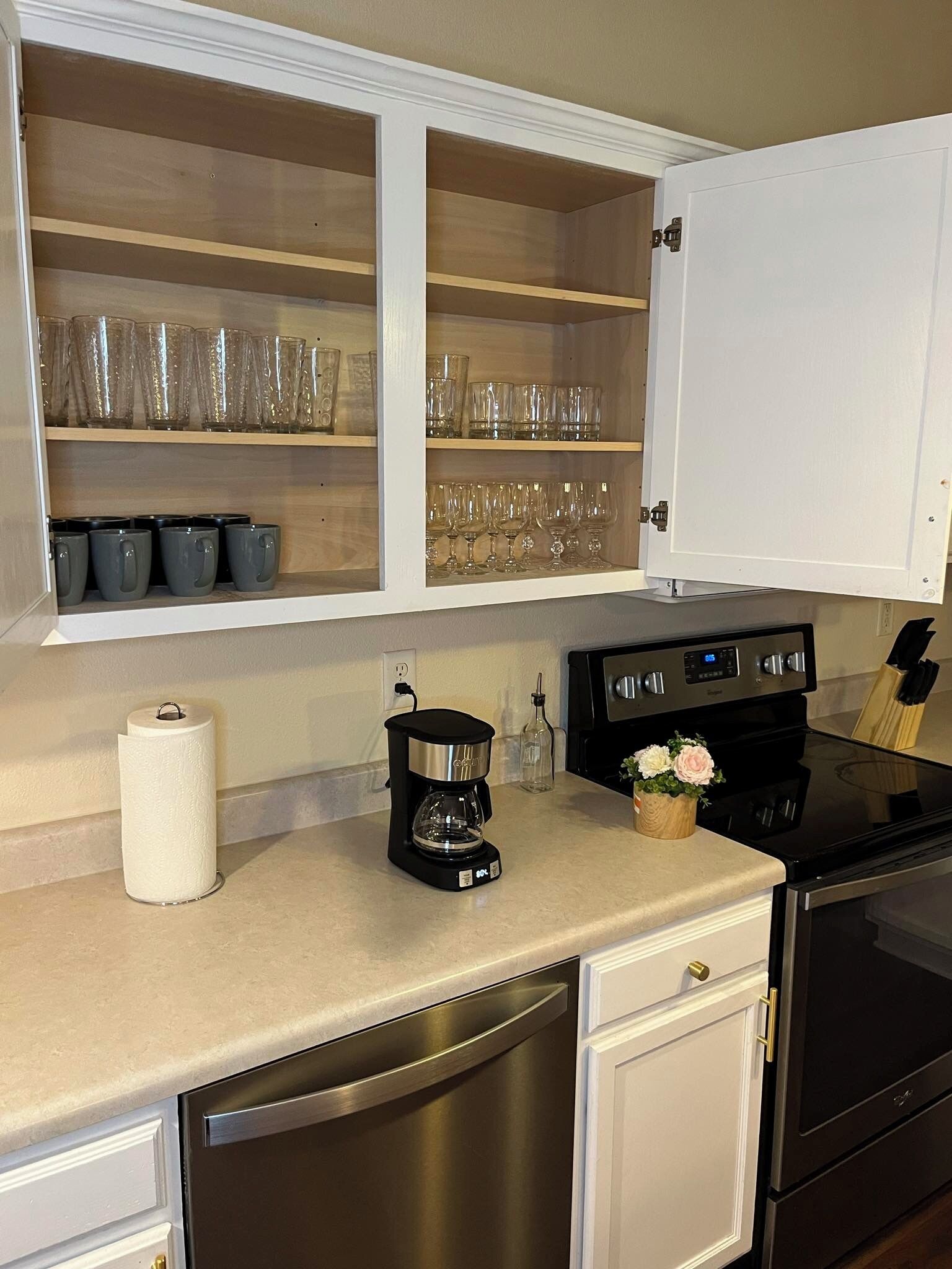 A kitchen with white cabinets, a coffee maker, a stove, and a dish rack.