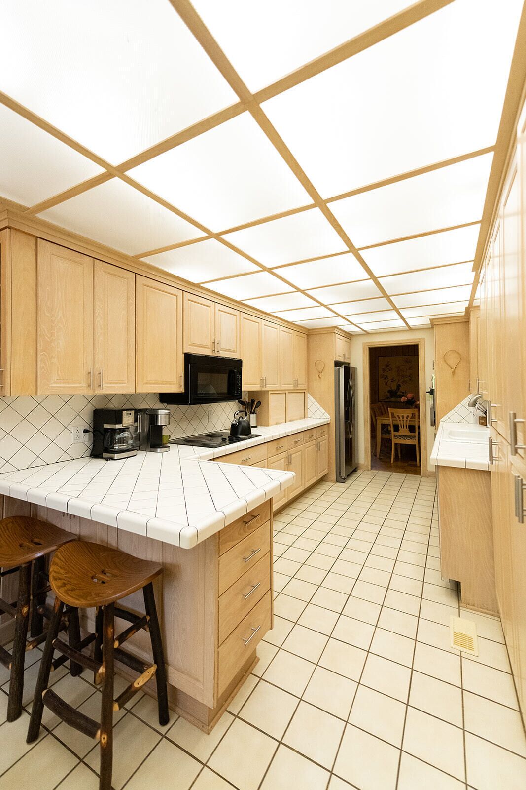 Una cocina con armarios de madera, una isla grande con taburetes, un microondas y un refrigerador.