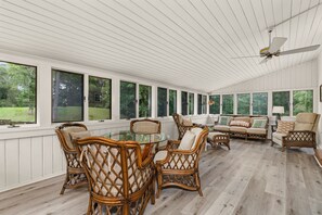 A sunroom with large windows, wicker furniture, and a ceiling fan.