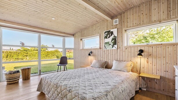 Ein Schlafzimmer mit einem großen Bett, zwei Fenstern, einem Sessel und einer Wandlampe.