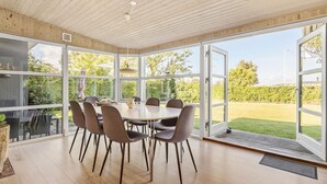 Ein Essbereich mit großem Tisch und Stühlen, einer Holzbalkendecke und großen Fenstern mit Blick auf einen Garten.