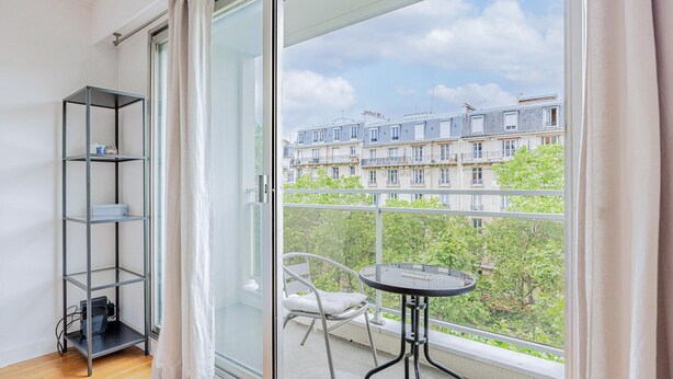 A balcony with a glass door, a metal shelf unit, a round table, and a chair.