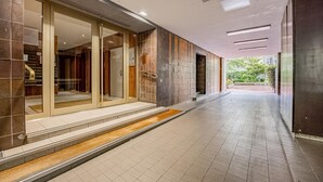 A modern hallway with glass doors leading to a room, tiled flooring, and a view of greenery outside.