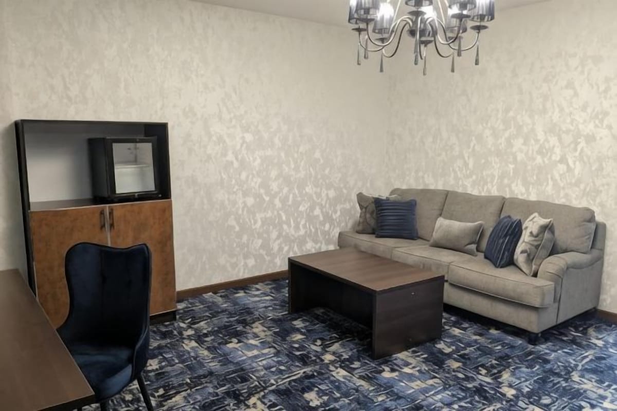 A living room with a sofa, a coffee table, a TV on a cabinet, and a patterned floor.