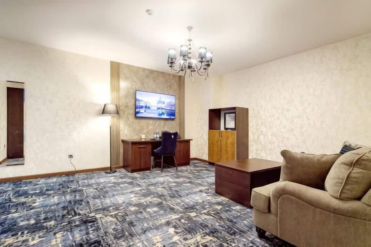 Quarto de hotel com cama grande, escrivaninha, televisão, lustre e sofá.