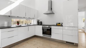Une cuisine moderne avec des armoires blanches, une hotte de cuisinière en acier inoxydable, un four et un évier placé sous une fenêtre.