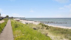 Un sentier côtier bordé d’une plage de sable, d’une jetée en bois et surplombant un ciel dégagé.