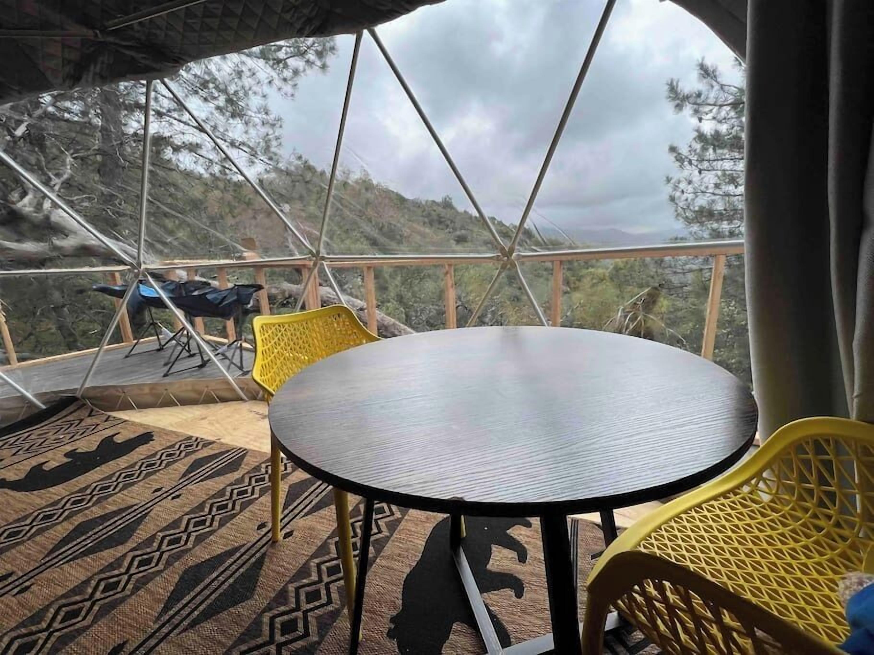 Een ronde tafel met stoelen, een kamerkleed met patroon en uitzicht op een berglandschap.