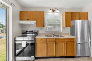 A modern kitchen with wooden cabinets, stainless steel appliances, and a window with blinds.