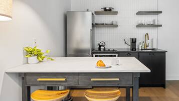 A modern kitchen with a white countertop, wooden stools, a stainless steel refrigerator, and black cabinets.