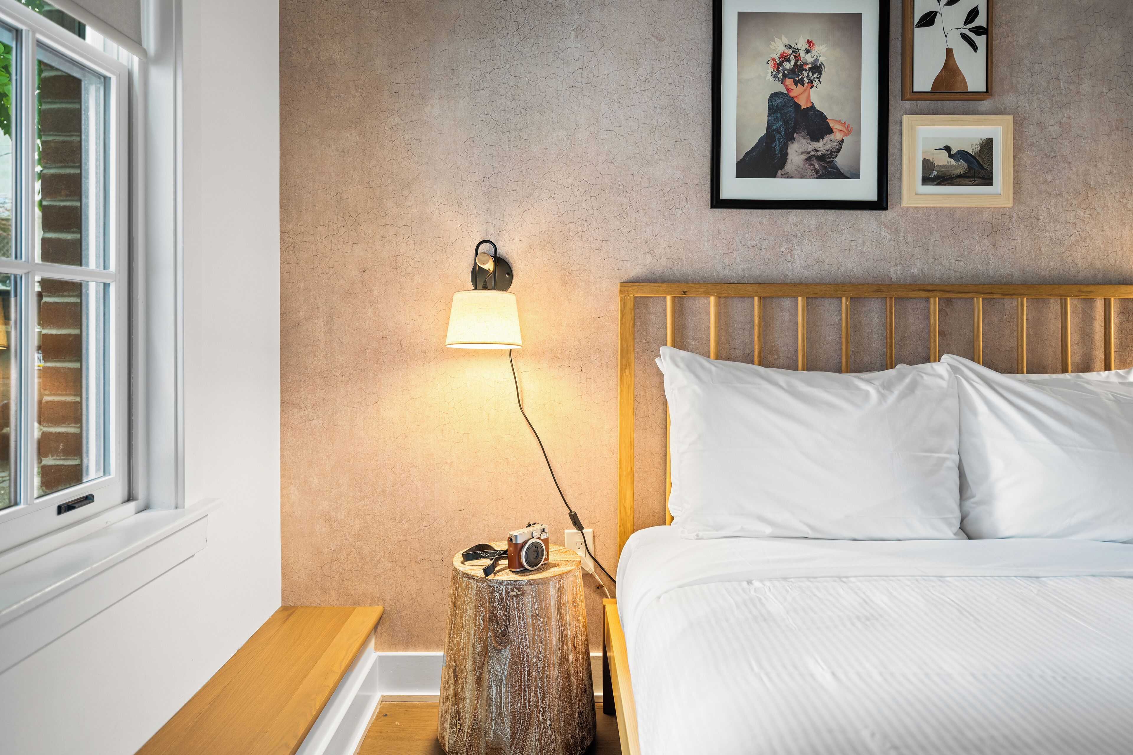 A bedroom with a wooden headboard, a bedside table with a lamp, and a camera on the table.