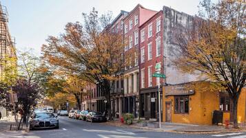Une vue de rue avec des immeubles, des voitures garées et des arbres d’automne.