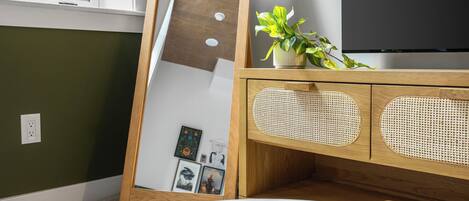 A room with a wooden cabinet, a flat-screen TV, a mirror, and a table with books and a coffee cup.